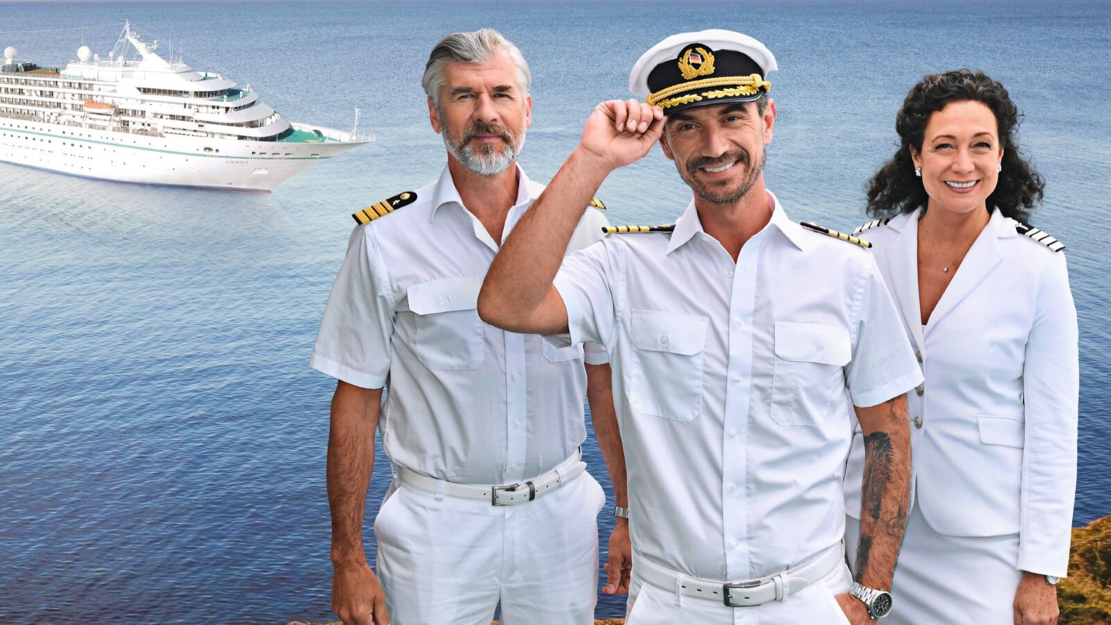 Drei Crewmitglieder in weißer Kapitänsuniform stehen lächelnd vor einem Kreuzfahrtschiff auf blauem Meer, einer hebt die Mütze. | © ZDF / Dirk Bartling