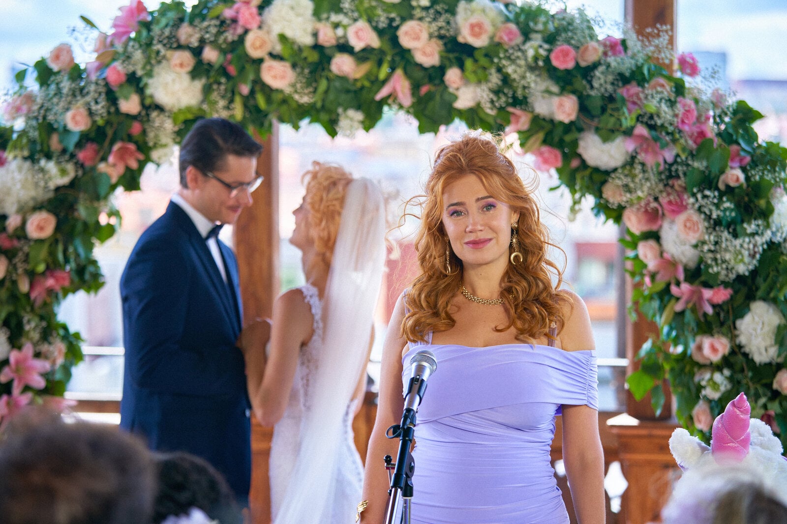 „My Ex - Die Liebenden“: Jan (Šimon Obdržálek) und Emma (Alli Neumann) stehen unter einem begrünten Traubogen mit weißen und rosa Rosen und schauen sich sehr verliebt an. Ivy (Palina Rojinski) steht seitlich vor ihnen vor einem Mikrophon und hält eine Rede. | © ZDF/Tomáš Mikule