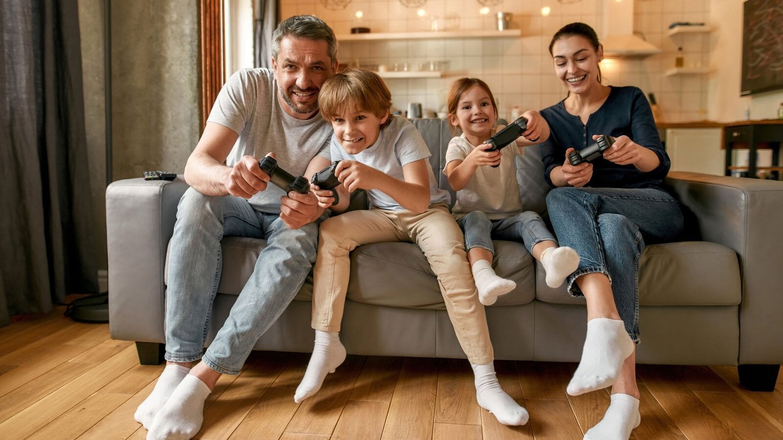 Vater, Mutter und zwei Kinder sitzen fröhlich auf dem Sofa und halten Controller in der Hand.  | © Svitlana / stock.adobe.com