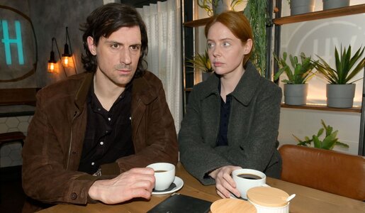 Ein dunkelhaariger junger Mann und eine rothaarige junge Frau sitzen ernst mit Kaffeetassen an einem Holztisch im Café. | © RTL / Rolf Baumgartner