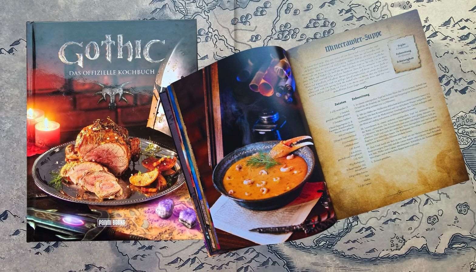 Offizielles "Gothic"-Kochbuch mit rustikaler Fleischplatte und dampfender Krabbensuppe, auf einer Landkarte liegend. | © Sabrina Forst